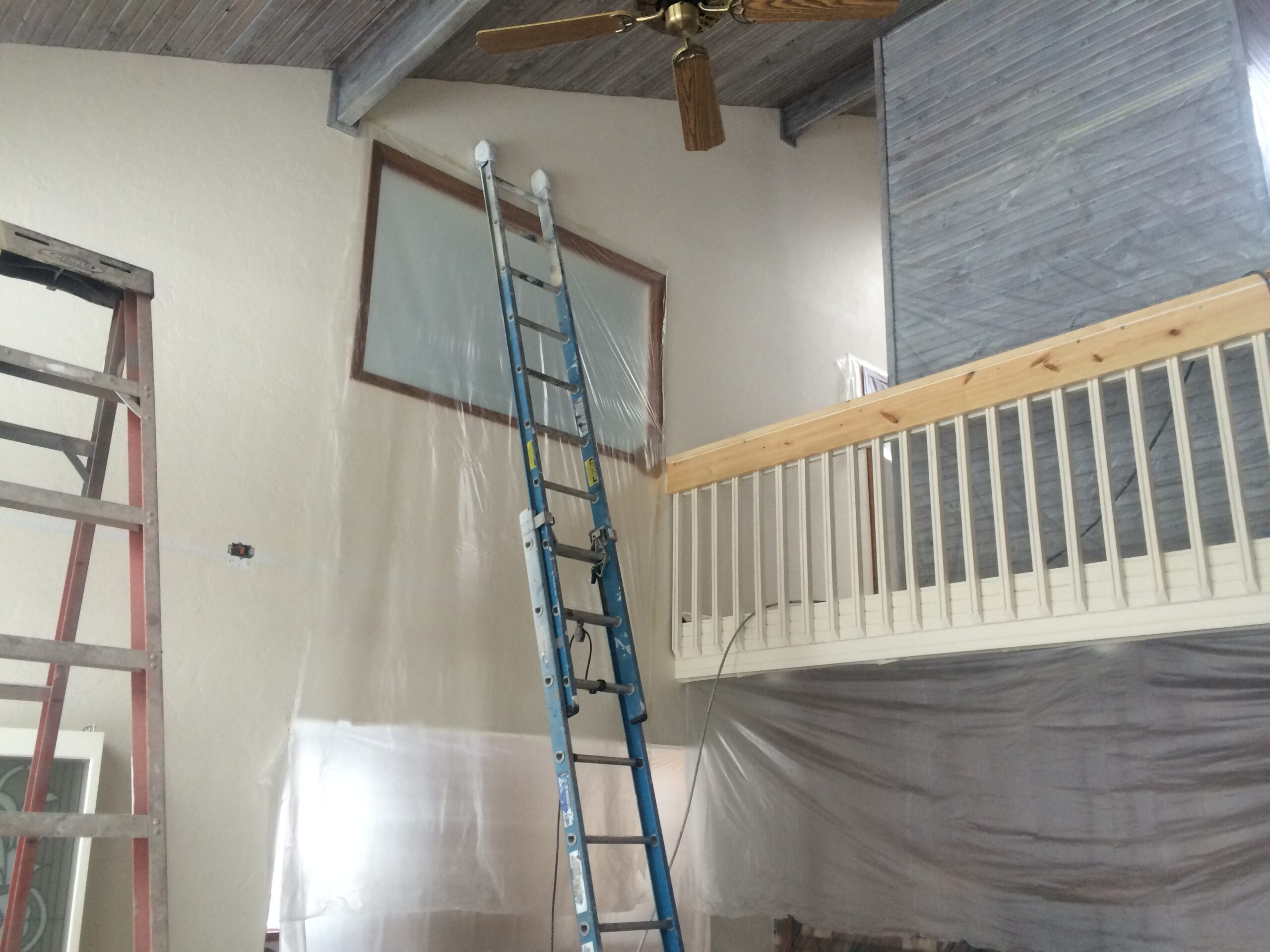 Interior room with bare walls, a ladder and drop cloths set up for surface preparation before painting
