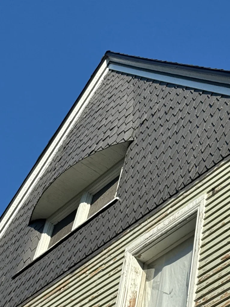 Gray shingled roof dormer and siding on a house, showing exterior exposure to Michigan weather