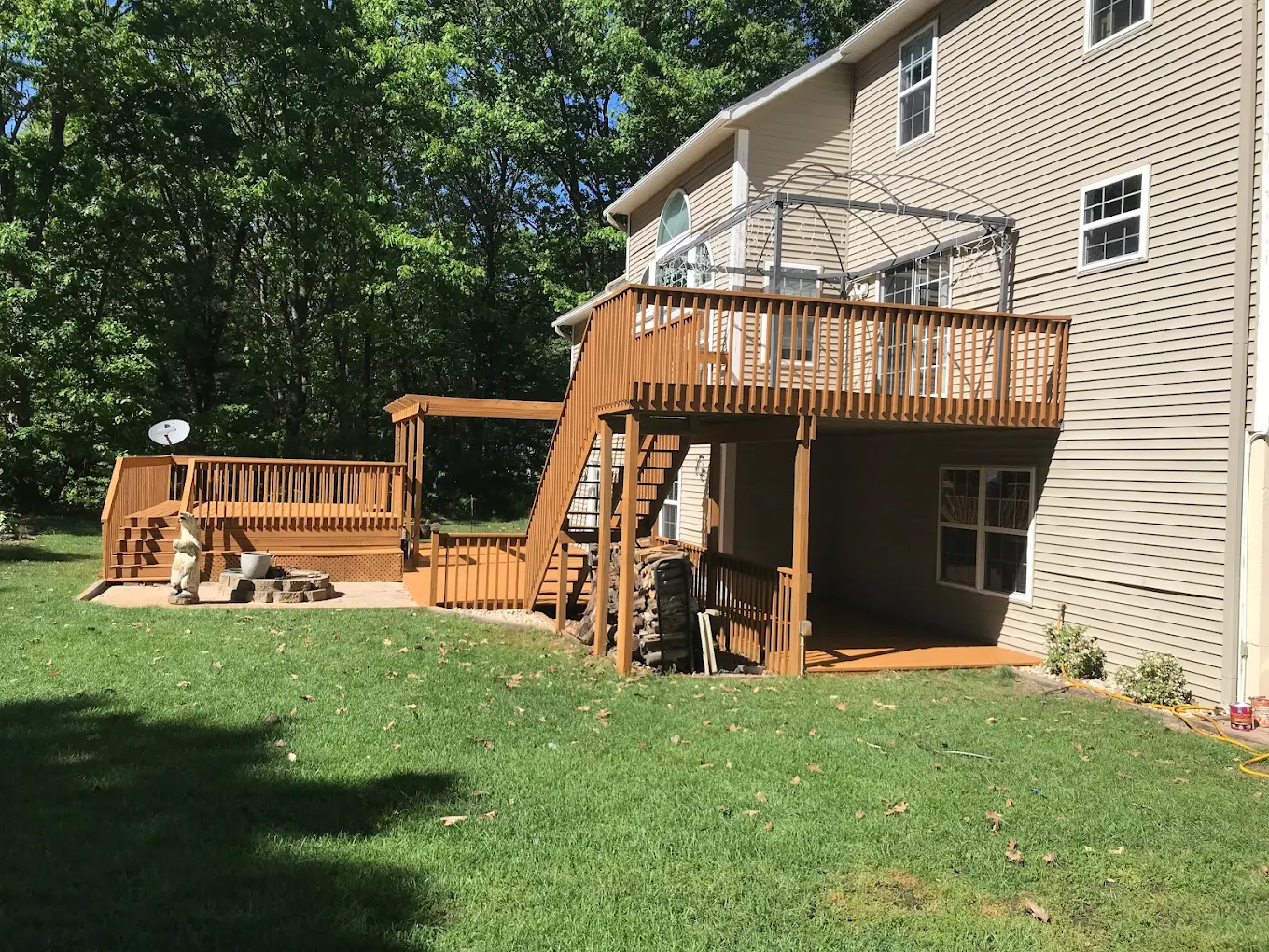 Wooden backyard deck with stairs and railings beside a two-story home with green lawn